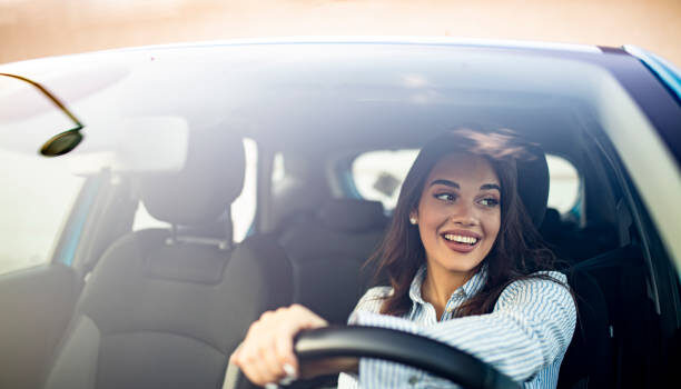 Happy woman driving a car and smiling. Cute young success happy brunette woman is driving a car. Portrait of happy female driver steering car with safety belt