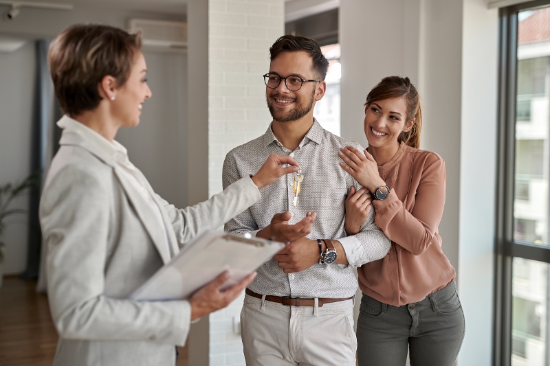Young happy couple receiving new house keys from real estate agent.
